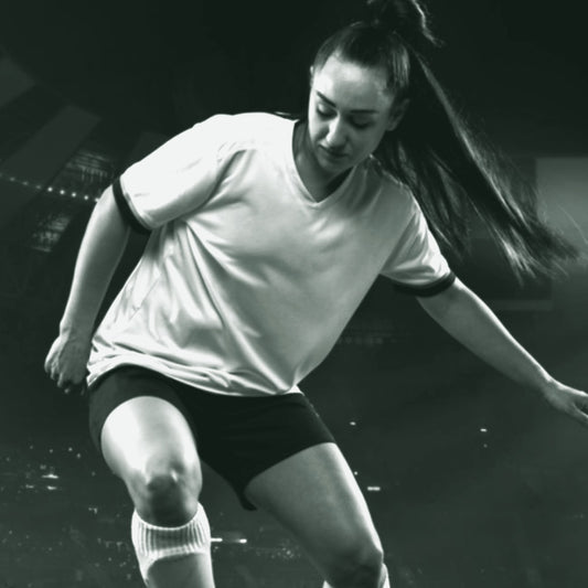 A female soccer player in action wearing a white soccer jersey with a logo on the chest and blue shorts. ThreaderPros women's custom soccer jersey.